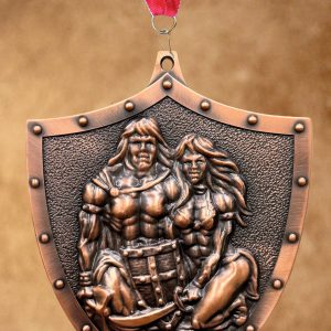 copper-colored shield-shaped medal hanging from a red, white, and blue striped ribbon, featuring an embossed relief of a muscular warrior couple in heroic poses